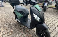 Frontansicht eines Piaggio Scooters in Grün-Schwarz, geparkt auf Pflastersteinen.