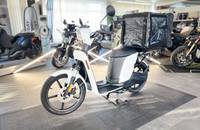 Außenansicht eines weißen Elektrorollers mit schwarzem Gepäckträger, präsentiert in einem Fahrgeschäft.