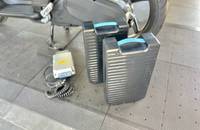 Seitenansicht des Elektrorrollers mit zwei Akkus und Ladegerät auf dem Boden.