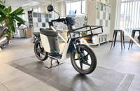 Ein weißer elektrischer Roller (scooter) mit schwarzem Akku und Gepäckträger steht auf einem gefliesten Boden in einem h