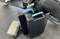 Nahaufnahme eines Elektroscooters mit zwei großen, schwarzen Akkus und einem kleinen Zubehörteil auf dem Boden.