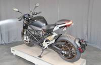 Seitenansicht eines schwarzen E-Motorrads, das auf einer Plattform ausgestellt ist.
