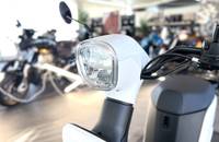 Nahaufnahme des weißen Scheinwerfergehäuses und des Lenkerbereichs eines Elektroscooters in einem Showroom.
