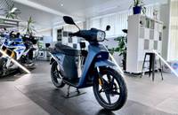 Ein blauer Elektroroller steht in einem hellen Showroom, aufgenommen aus der Seitenansicht.