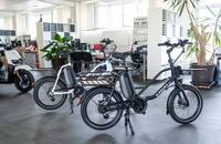 Mehrere E-Bikes, darunter ein schwarzes Lastenrad, in einem hellen Showroom.