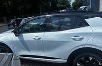 Seitenansicht eines weißen KIA Sportage, geparkt vor einem Autohaus.
