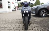 Frontalansicht des elektrischen Motorrads RAY 7.7 vor einem Autohaus.