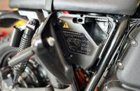 Nahaufnahme des Seitenfachs des Motorrads mit Schließmechanismus und Anleitung zum Ersatzschlüssel.