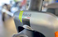 Nahaufnahme des Logos "Askoll" mit farbigen Streifen und Carbon-Muster auf einem Fahrzeugdetail.