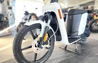 Front-Ansicht eines weißen elektrischen Scooters mit sichtbarem Vorderrad, Bremsanlage und Seitenverkleidung.