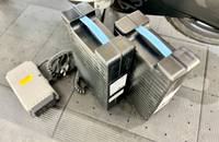Zwei große Akkus (Askoll) und ein kleines elektronisches Bauteil liegen vor einem Elektrofahrrad.