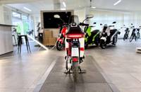 Ein weißer Elektroroller wird in einem hellen Showroom vor mehreren anderen Motorrädern präsentiert.