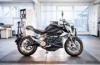 Seitenansicht eines schwarzen Elektro-Motorrads in einem modernen Showroom.