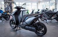Seitenansicht eines grauen, elektrischen Motorrollers in einem Showroom.