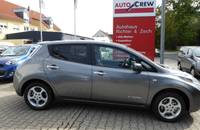 Seitenansicht eines grauen Nissan Leaf Elektroautos auf einem Parkplatz vor einem Autohaus.