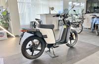 Ein weißer Elektroroller steht in einem Showroom und wird von einer Dreiviertel-Ansicht gezeigt.