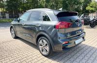 Ein grauer KIA E-Niro Electric wird von der Seite und hinten vor einem Autohaus abgebildet.