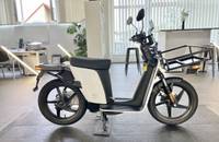 Seitenansicht eines weißen und schwarzen E-Scooters, der in einem hellen Showroom steht.