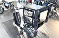 Seitenansicht eines weißen Elektrorollers mit einem großen, schwarzen Seitengepäckträger.