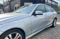 Silberner Mercedes-Benz C-Klasse Seitenansicht vor einem Autohaus.