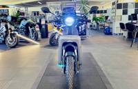 Ein grauer Elektroroller steht in einem hellen Showroom, umgeben von weiteren Motorrädern.