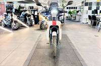 Ein weißer Elektroroller steht im Showroom. Im Hintergrund sind weitere Motorräder und das Verkaufsambiente zu sehen.