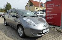 Außenansicht eines grauen Nissan Leaf Elektroautos, das auf einem Parkplatz vor einem Autohaus steht.