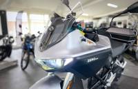 Frontansicht eines silbernen E-Motorrads mit Windschutzscheibe und Scheinwerfer.