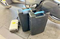 Nahaufnahme eines Elektroscooters mit zwei extern platzierten Akkus und einem Ladegerät auf dem Boden.