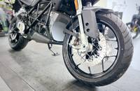 Nahaufnahme eines silbernen Elektro-Motorrads, die den vorderen Reifen, die Bremsscheibe und den Rahmenbereich zeigt.
