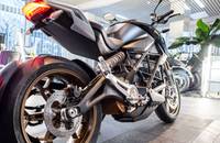 Seiten- und Heckansicht eines schwarzen und goldfarbenen E-Motorrads in einem Autohaus.