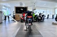 Ein dunkler Roller steht in einem hellen Showroom mit mehreren anderen Motorrädern im Hintergrund.