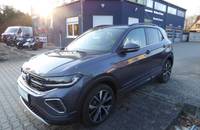 Außenansicht eines VW T-Cross in Rauchgrau Metallic vor einem Autohändler.
