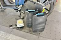 Außenansicht eines blauen E-Scooters mit zwei Akkus auf dem Boden.