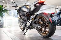 Dunkelgraues Motorrad im Dreiviertel-Heckblick mit goldfarbigem Rad.