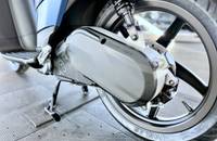 Nahaufnahme des hinteren Bereichs eines Motorrads, die das Rad, den Auspuff und den Seitenständer zeigt.