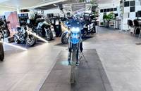 Ein blaues Motorrad steht in einem hellen Showroom mit weiteren Motorrädern im Hintergrund.