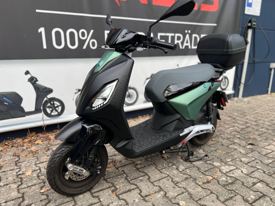 Außenansicht eines Piaggio Scooters in Grün-Schwarz vor einem Autohaus.