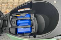 Nahaufnahme des Stauraumfachs eines Piaggio-Rollers mit eingebauter blauer Batterie.