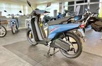 Seitenansicht eines hellblauen Elektro-Rollers in einem Showroom.