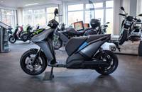 Seitenansicht eines grauen elektrischen Scooters in einem gut beleuchteten Showroom.