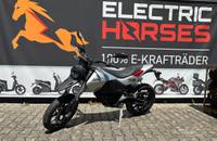 Silbernes E-Motorrad auf Kopfsteinpflaster vor dem Banner des Autohauses Electric Horses.