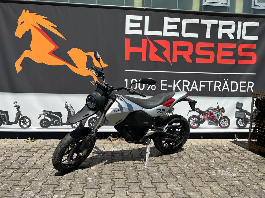Silbernes E-Motorrad auf Kopfsteinpflaster vor dem Banner des Autohauses Electric Horses.