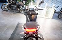 Aufsicht von hinten auf ein schwarzes E-Motorrad in einer Ausstellungshalle.