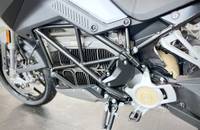 Nahaufnahme der Seitenansicht eines elektrischen Motorrads, die den Rahmen, den Motorblock und das Vorderrad zeigt.