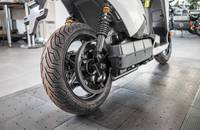 Hinterrad und Unterbau eines weißen E-Scooters in einer Showroom-Umgebung.
