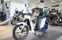 Weißer elektrischer Roller (eSPro) in Dreiviertelansicht, präsentiert in einem Showroom.