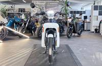 Eine weiße Elektro-Motorroller steht in einem Showroom, umgeben von anderen Motorrädern.