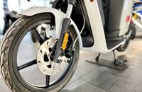 Nahaufnahme des vorderen Rades und der Bremsscheibe eines weißen Elektroscooters.