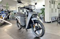 Frontale Außenansicht eines mattschwarzen Elektro-Scooters in einem hellen Showroom.